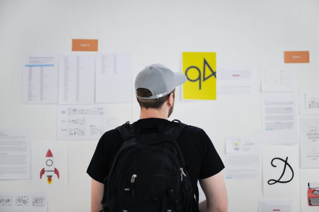 Man with cap and backpack looking at white board